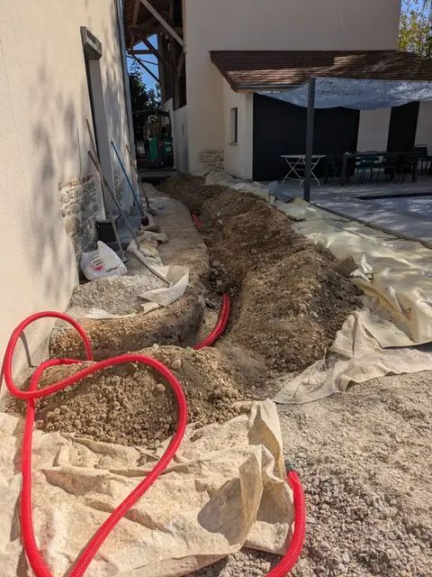 Tranchée ouverte avec gaines rouges pour le passage des câbles lors d'un chantier photovoltaïque à Maubec (38)